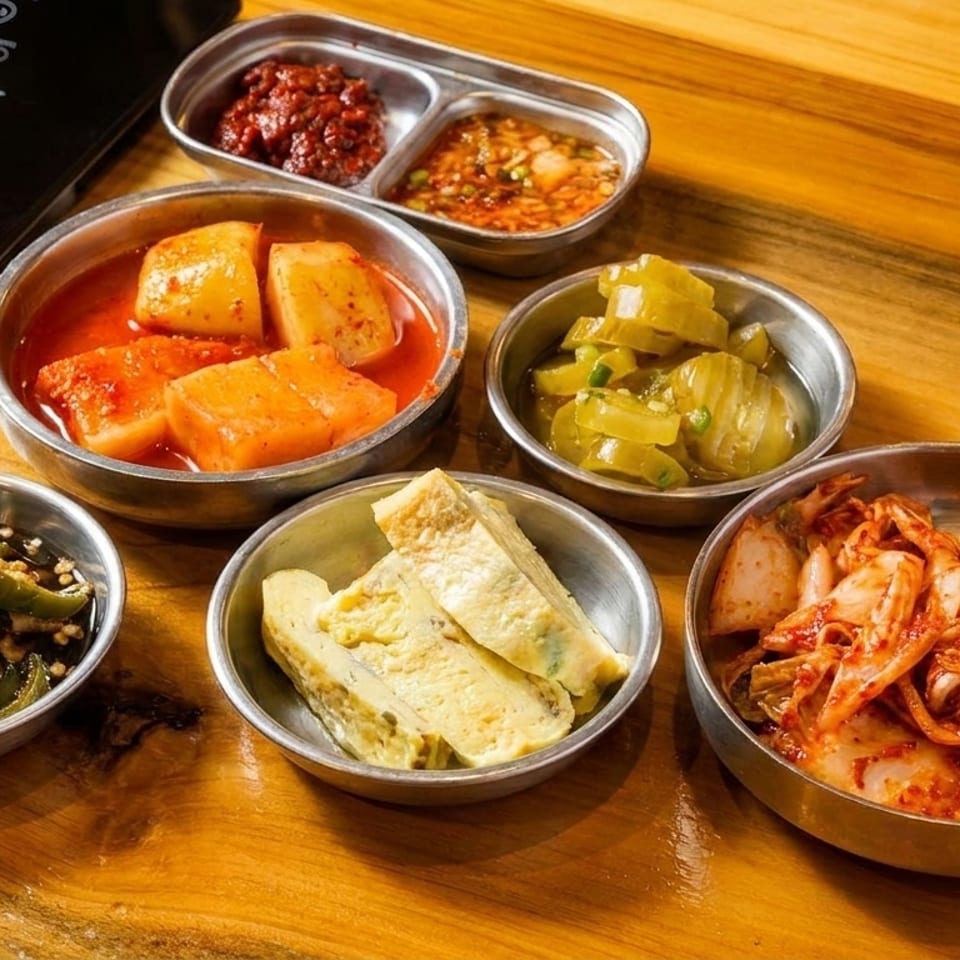 Assortment of Korean banchan side dishes including kimchi, pickled radishes, and egg rolls on a wooden table.